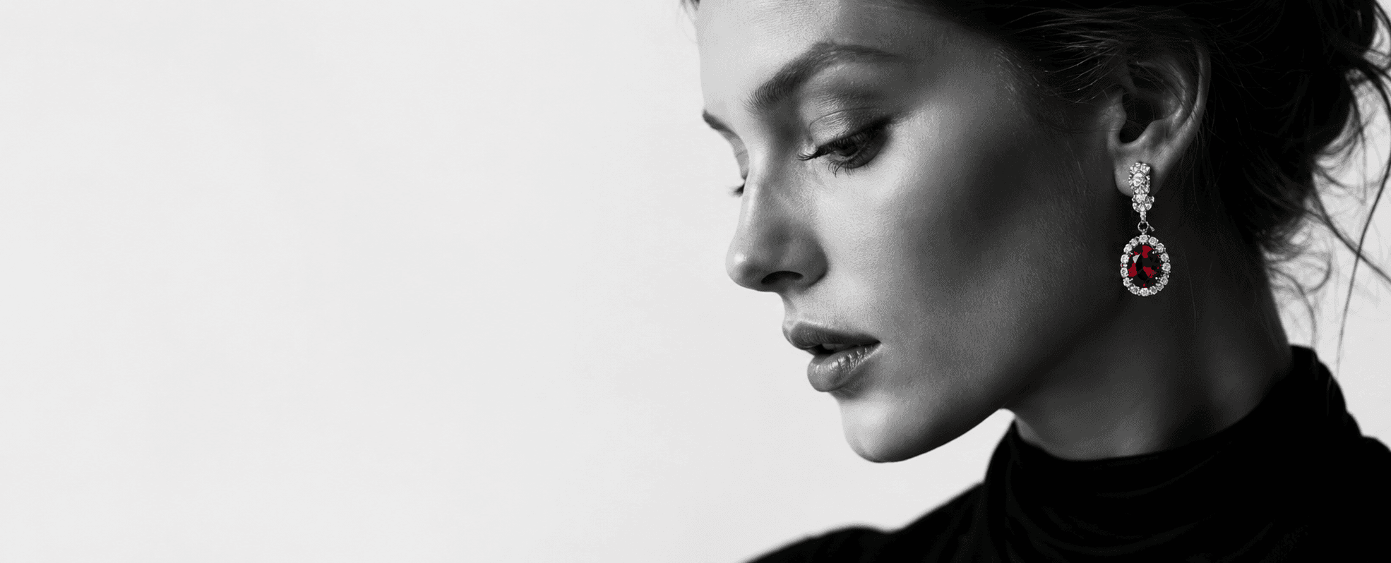 Side profile of an elegant woman, hair swept back, wearing a diamond-halo drop earring set with a deep-red spinel